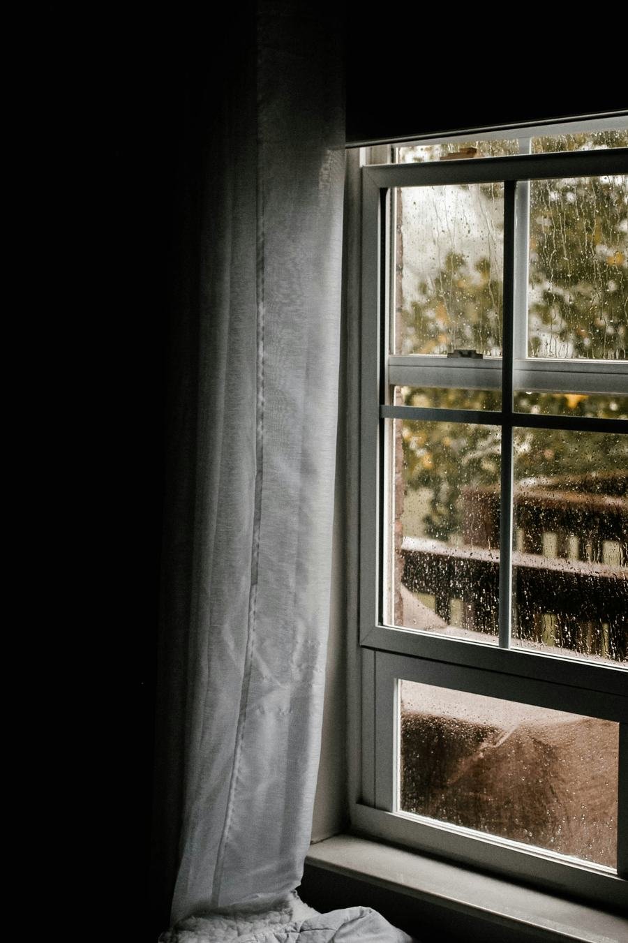 Ventana con lluvia y cortina, vista íntima de un interior